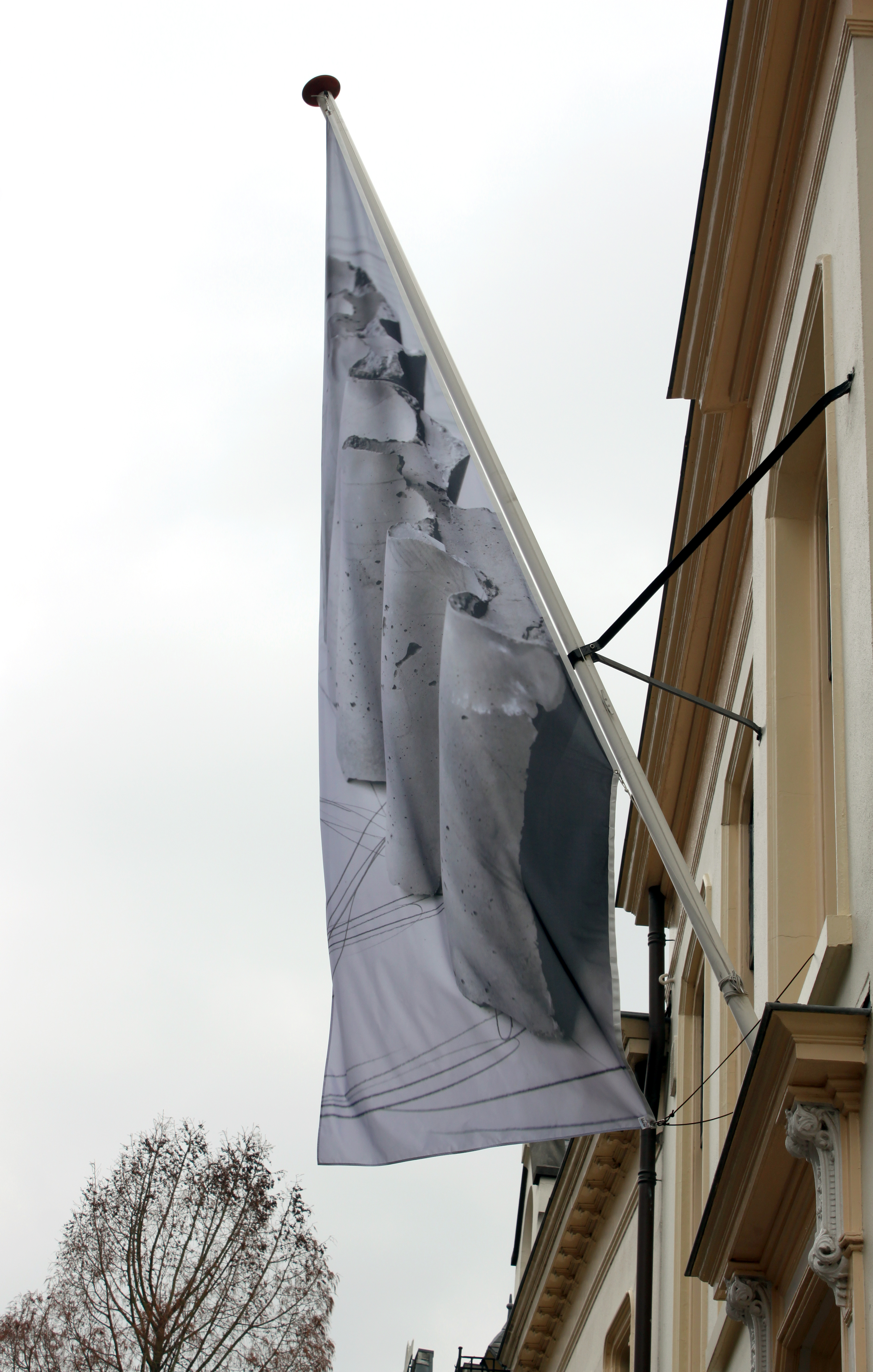 vlag met daarop een golvend betonobject hangt aan de mast aan de gevel